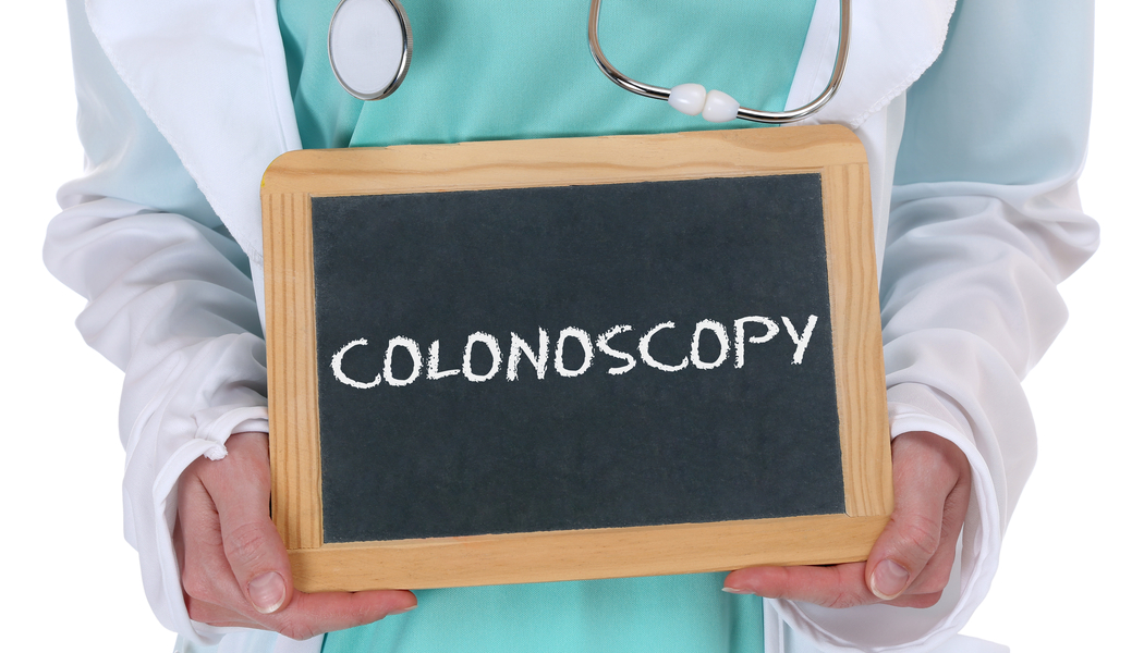 A female woman doctor wearing a white coat and stethoscope holding a sign that says Colonoscopy