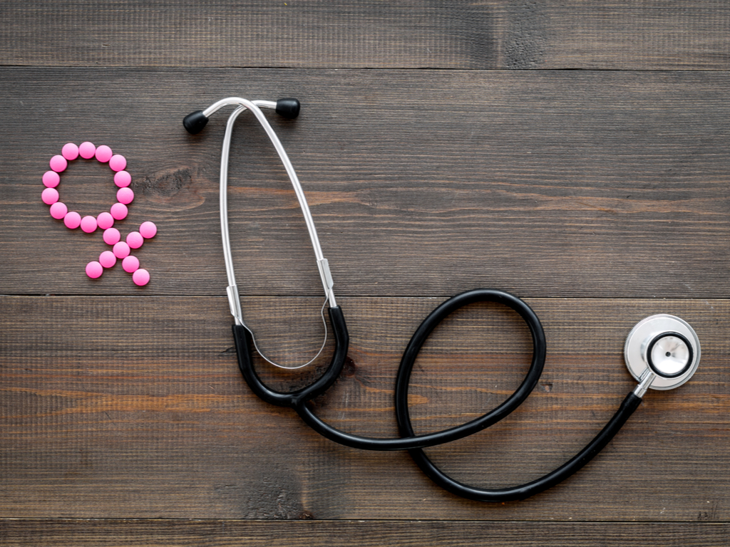A stethoscope laying on a wooden table next to a menopause symbol shaped from pink pills