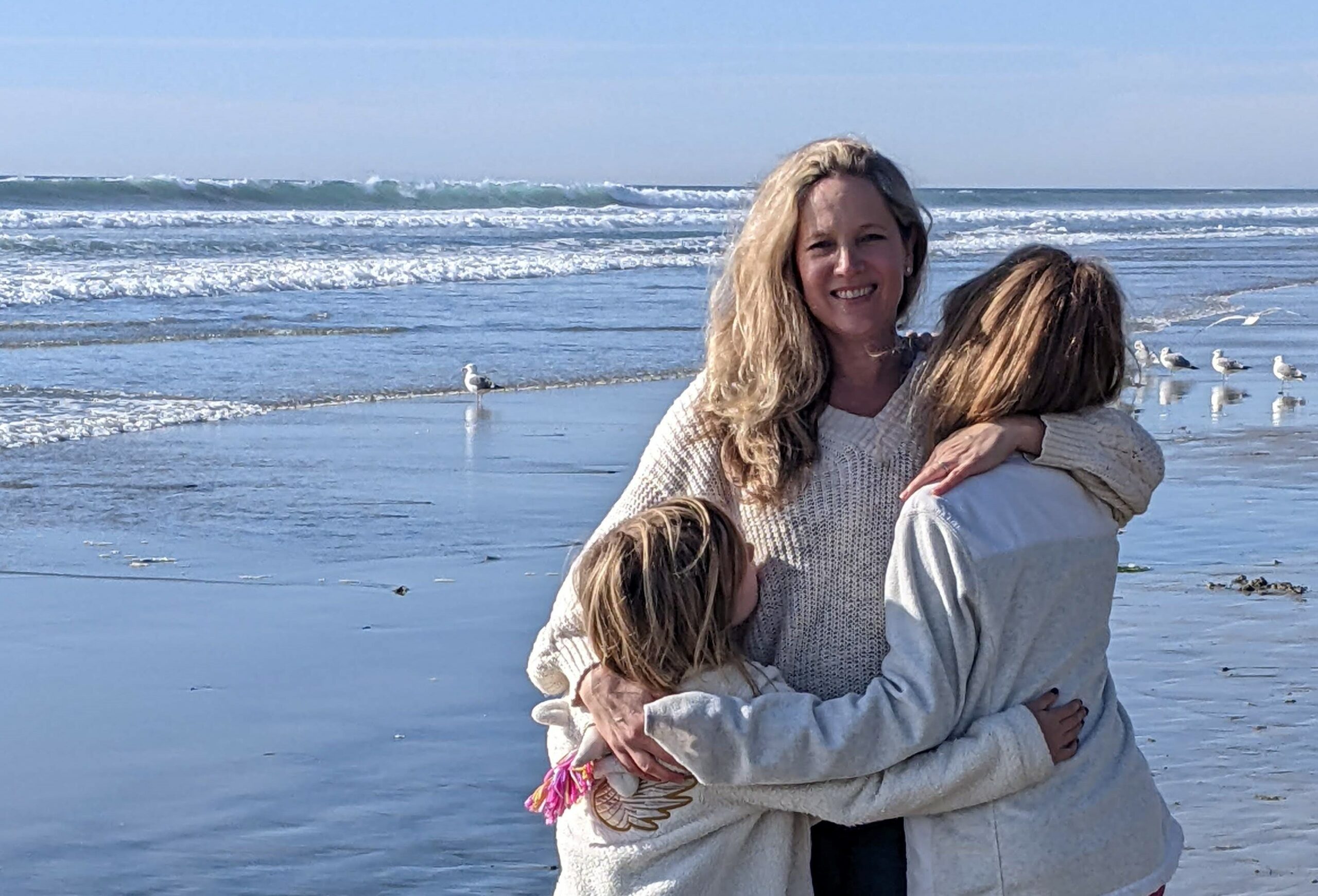 Journalist and writer Madeleine Collins hugging her two daughters at the beach