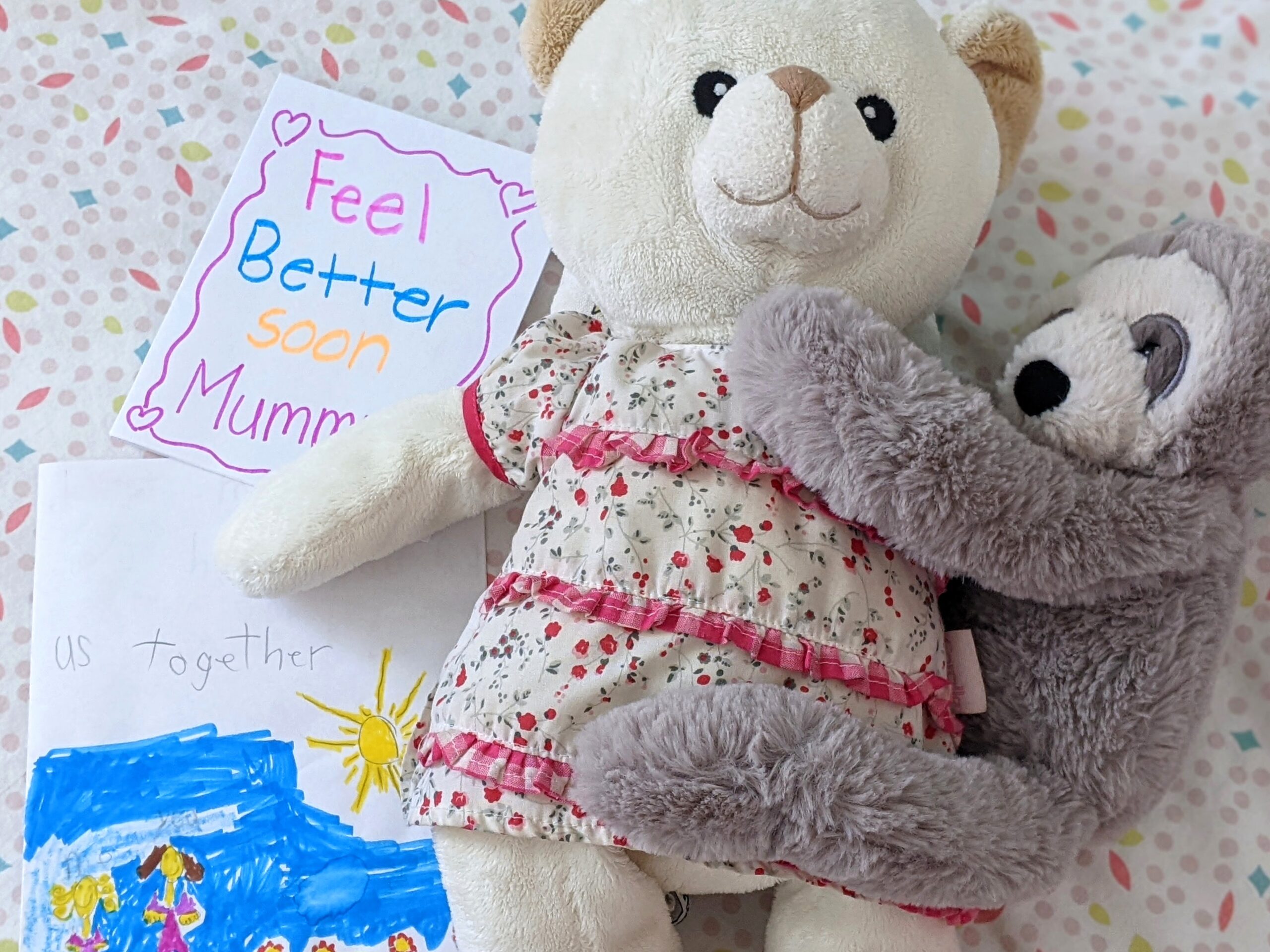 Two cuddly toy teddies hugging next to letter saying Feel Better Soon Mommy
